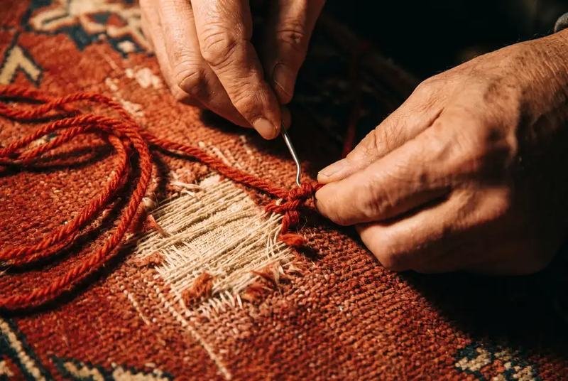 Mains renouant la laine sur une zone de tapis mangée par les mites, trame à nu