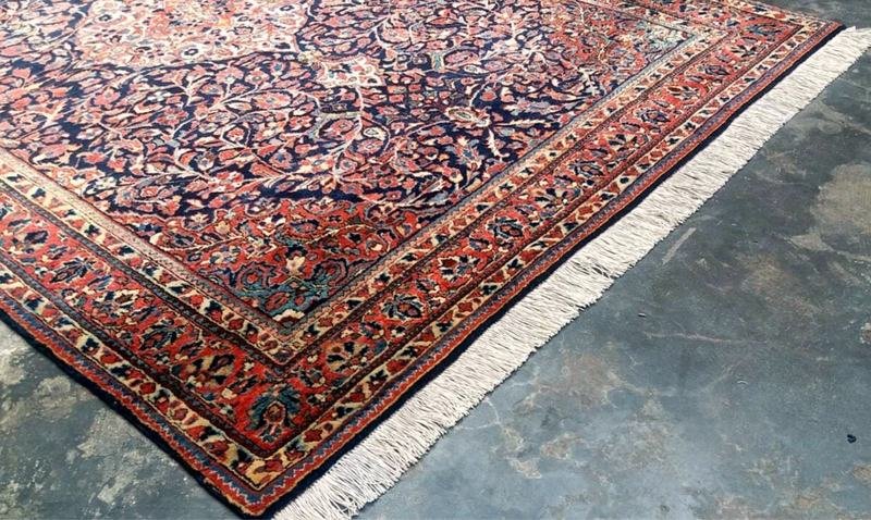 Tapis persan posé au sol de l’atelier, angle et franges visibles